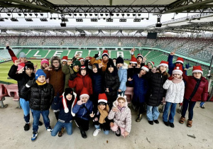Grupowe zdjęcie na ostatnim tarasie na tle napisu "Legia" ułożonego z krzesełek w kolorze białym.