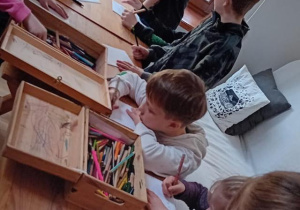 Uczniowie stoją przy stole i tworzą książeczkę klasową.