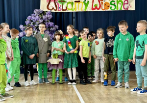 Klasa 1a, ubrana w zielone kolory, wita wiosnę wierszem.