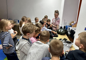 Uczniowie znajdują się w Strefie Szycia, stoją wokół stołu krawieckiego i oglądają materiały.