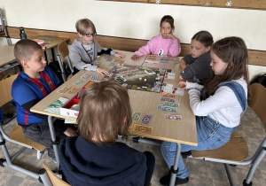 Uczniowie z klas 3a i 3b siedzą przy stoliku i grają w Monopoly.