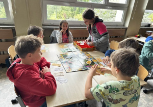 Uczniowie z klas 3a i 3b siedzą przy stoliku i grają w Monopoly.