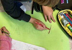 Uczniowie tworzą plakat z okazji "Światowy Dzień Zwierząt" na kartonie w kolorze zielonym.