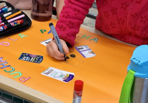 Dziewczynka koloruje na czarno psią łapkę, którą naszkicowała na plakacie.