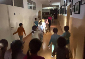 Nocne zwiedzanie szkoły, dzeci idą szkolnym korytarzem.