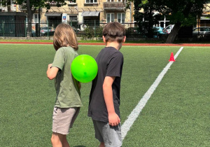 Chlopcy, odwróceni do siebie plecami, przenoszą balon.