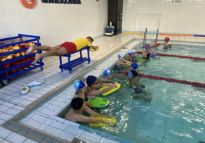 trener pokazuje uczniom prawidłowe ruchu rąk podczas pływania.