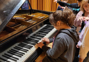 Studio nagrań dźwiękowych - dzieci stoją cierpliwie w kolejce do zagrania na studyjnym fortepianie. Przy klawiaturze Julia Szewczuk.