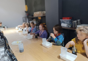 Uczniowie siedzą przy długim stole i przygotowuja się do eksperymentu.