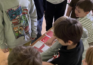 Grupa uczniów próbuje rozwiązać zadanie - wskazanie polskiej flagi wśród symboli narodowych innych krajów.