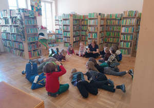 Uczniowie słuchają książki, która czyta dla nich pani z biblioteki.