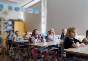 Uczniowie z klasy 1a siedzą w ławkach i oglądają prezentację.