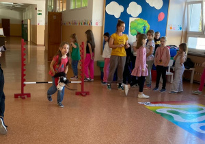 Uczennica rozpoczęła bieg przez przeszkody. Pozstali uczniowie czekają na swoją kolej.