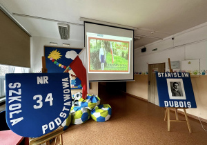 Na korytarzu stoi duża granatowa tarcza szkoły oraz zdjęcie patrona szkoły, Stanisława Dubois.