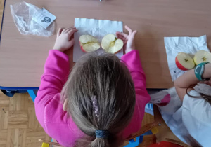 Uczennice siedzą w ławce i patrza na połowki swoich jabłek.