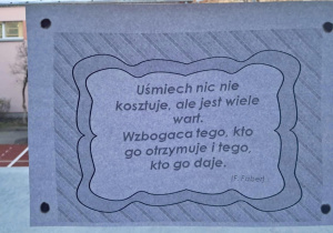 Na szkolnym korytarzu, w oknie wisi przysłowie "Uśmiech nic nie kosztuje, ale jest wiele wart. Wzbogaca tego, kto go otrzymuje i tego, kto go daje".