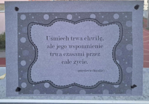 Na szkolnym korytarzu, w oknie wisi przysłowie "Uśmiech trwa chwilę, ale jego wspomnienie trwa czasami przez całe życie".