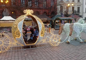 Uczniowie znajdują się na rynku miasta i pozują w karocy do grupowego zdjęcia.