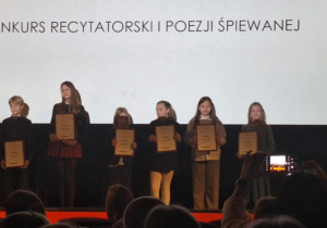 Zwycięzcy w Konkursie Recytatorskim i Poezji Śpiewanej stoją na scenie i prezentują dyplomy.