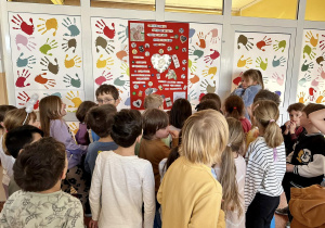 Uczniowie stoją przy plakacie, który wisi na szkolnym korytarzu.