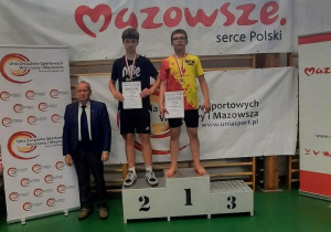 Adam stoi na podium podczas dekoracji medalami i dyplomami.