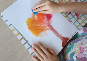 Uczennica rozciera gąbką drzewo namalowane w jesiennej odsłonie.