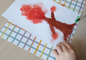 Uczeń maluje farbami drzewo w jesiennej odsłonie.