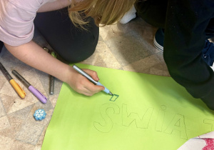 Uczniowie tworzą plakat z okazji "Światowy Dzień Zwierząt" na kartonie w kolorze zielonym.