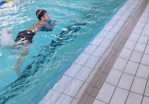 Uczniowie pływają w basenie. Dzieci używają desek do pływania..