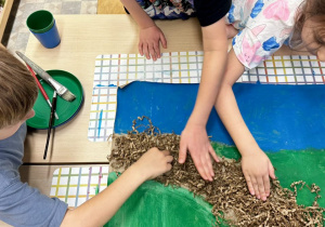 Uczniowie przyklejają tekturowe wypełnienie, które imituje ścieżkę w parku.