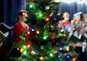 Na pierwszym planie stoi choinka, na drugim stoi chór.