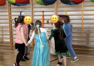 Uczennice tańczą w kółku pod dekoracją z kolorowych parasoli.