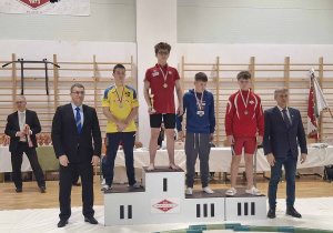 Nasz uczeń, Adam Gostkowski, stoi na podium wsród pozostałych zawodników, po dekoracji medalami i w ręku trzyma puchar.