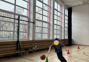 Chłopiec kozłuje piłką do koszykówki w slalomie.