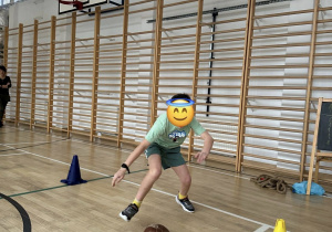 Chłopiec toczy piłkę lekarską w slalomie.