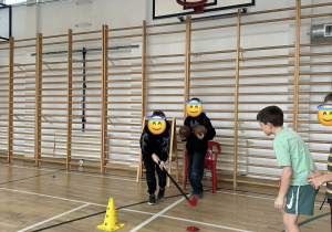 Uczniowie toczą woreczek kijem w slalomie.