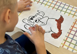 Uczeń maluje palcami kolorowankę z podobizną kundelka, która do złudzenia przypomina zakochanego kundla.