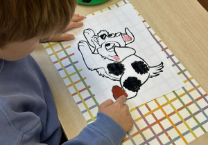 Uczeń maluje palcami kolorowankę z podobizną kundelka, która do złudzenia przypomina zakochanego kundla.