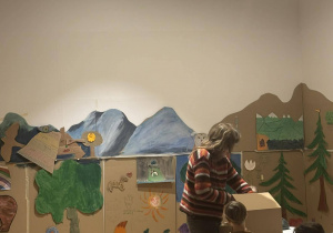 Uczniowie, siedząc przy stolikach, z zainteresowaniem czekają na pokaz zabawek.