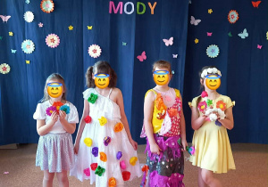 Dzieci prezentują piękne i kolorowe stroje stojąc na tle napisu dekoracyjnego "Wiosenny Pokaz Mody".