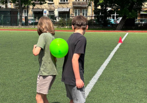 Chlopcy, odwróceni do siebie plecami, przenoszą balon.