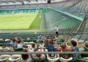 Uczniowie siedzą na trybunach i słuchają historii Klubu Legia Warszawa.